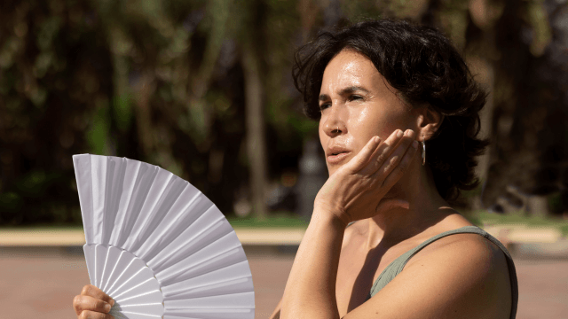 A person in the sun holding a paper fan to prevent overheating