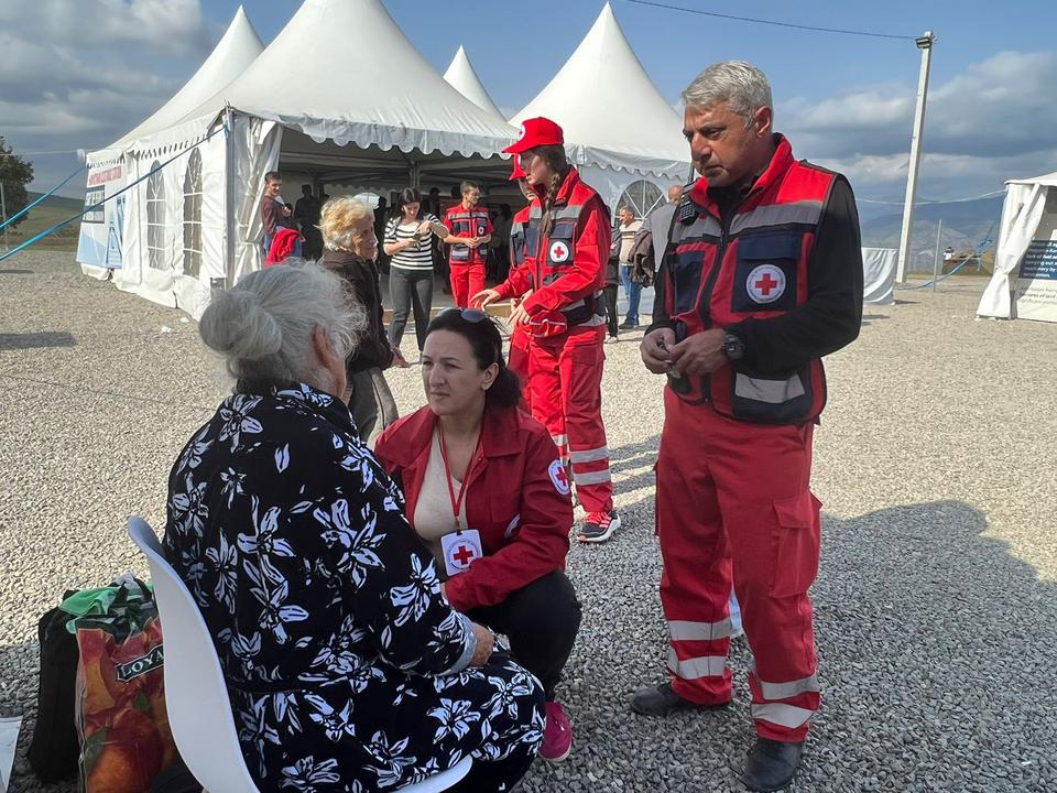 A group of people in red cross uniforms tend to a seated older woman