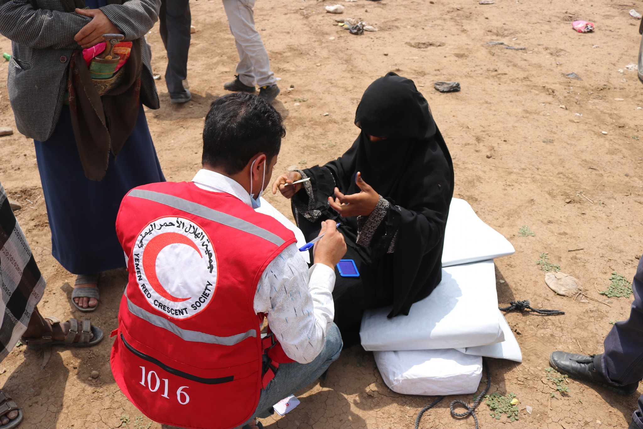 A person in a red vest and a person in black clothing sitting on the ground