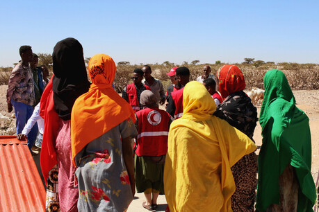 A group of people standing around a small group of people wearing Red Crescent vests