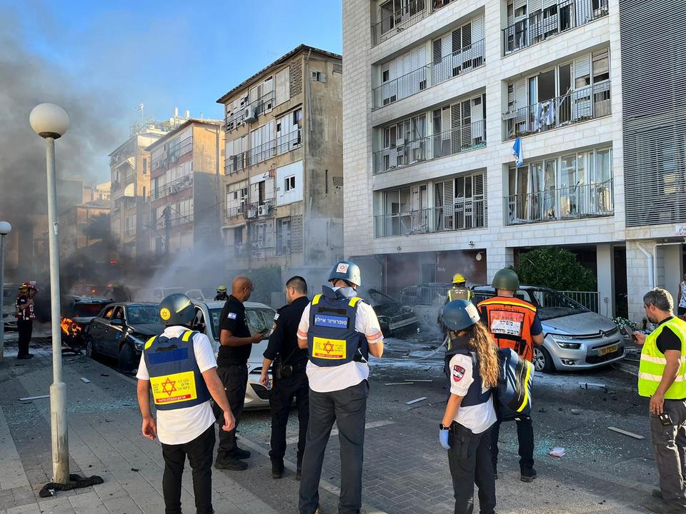 A group of people standing in front of buildings with a fire in the background