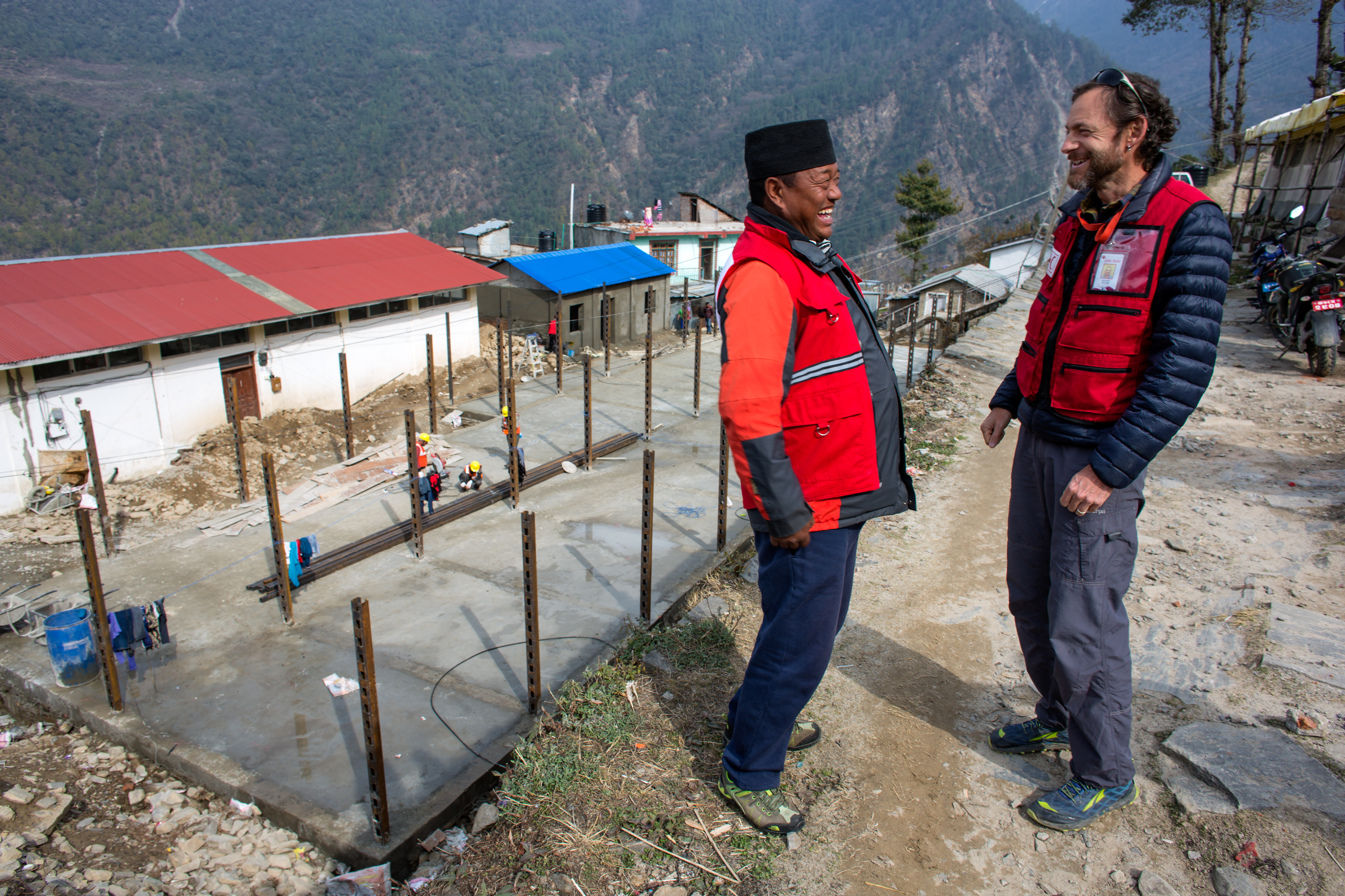 Two men talking in a rural area with mountains and construction in the background