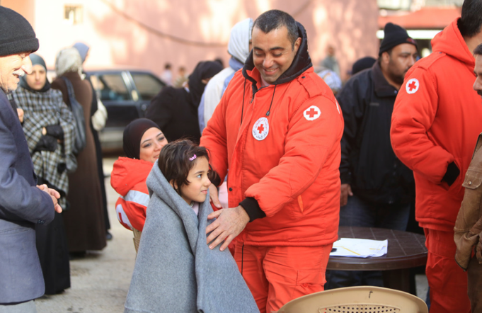 Man in a Red Cross uniform covers a child in a blanket