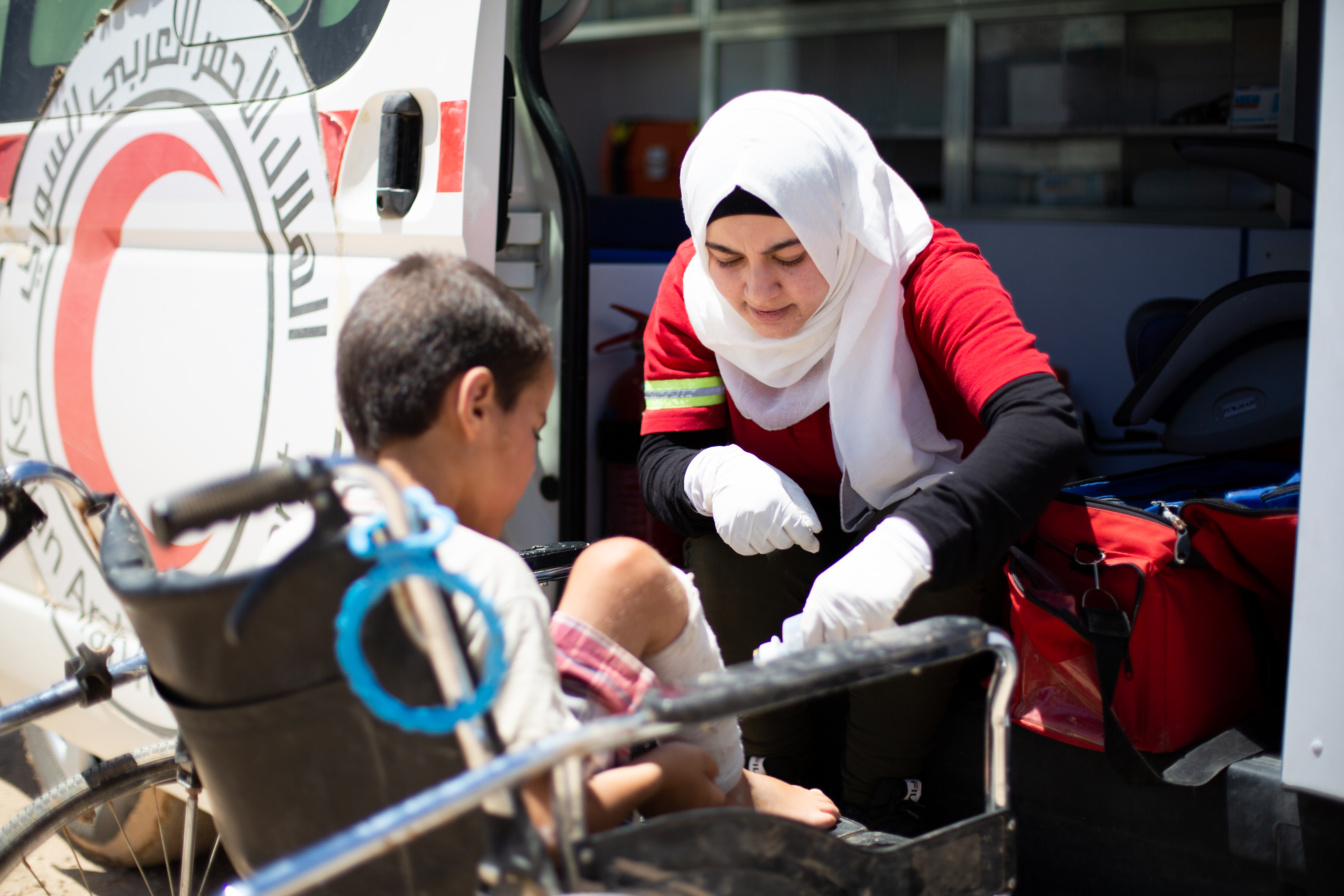 A woman wearing a white headscarf and red uniform helps a child in a wheelchair